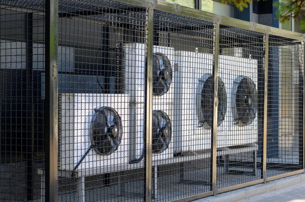 Air conditioning compressor system on a modern building protected by a metal fence.