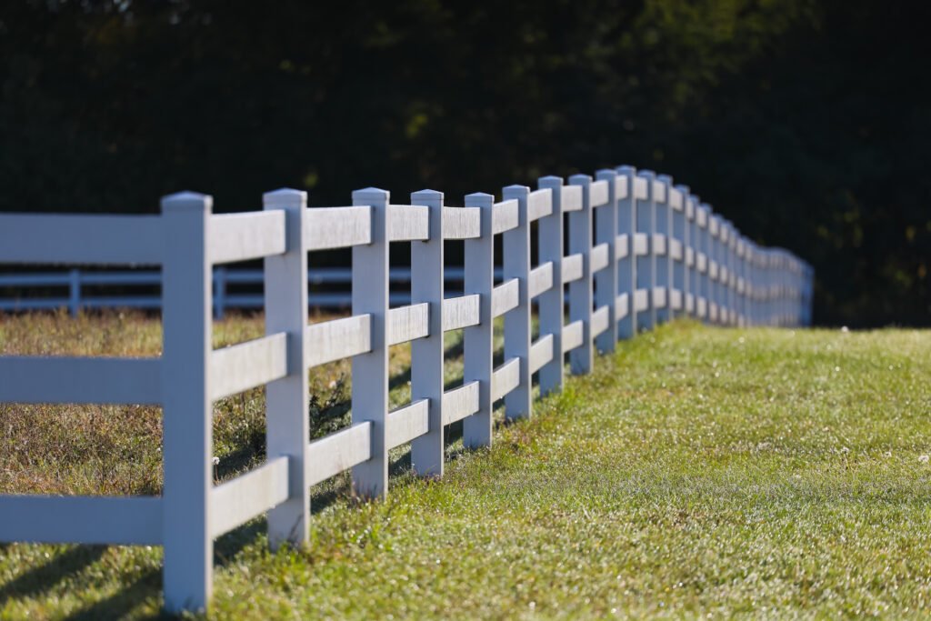 Corner view of a white wooden horse fence fading off in the distance with green grass.