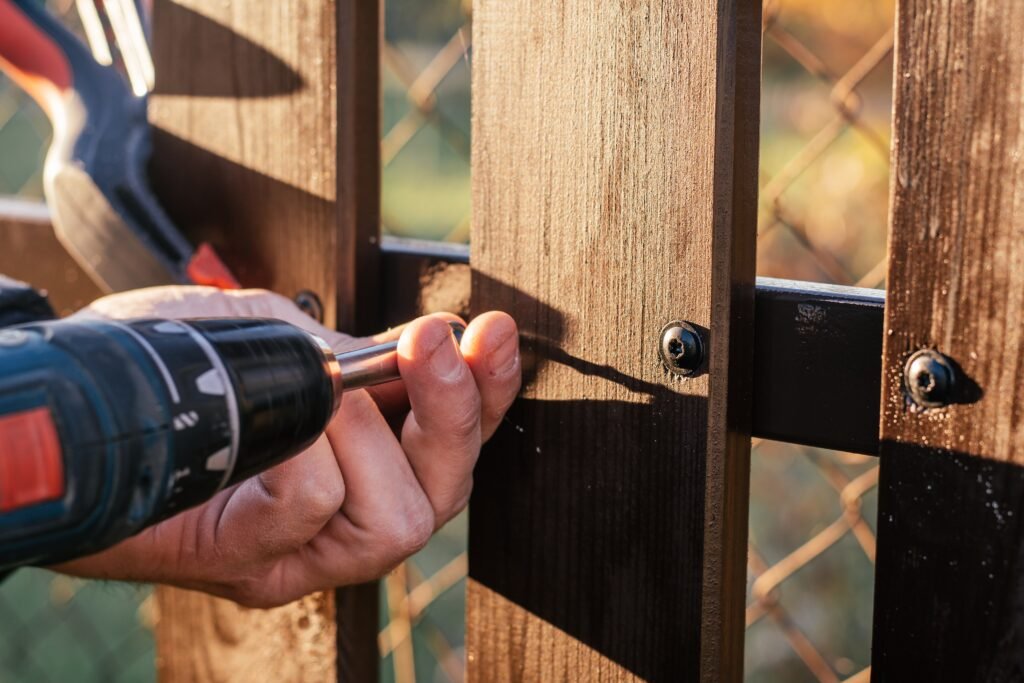 Hand of carpenter holding stud driving machine putting screw into wooden plank