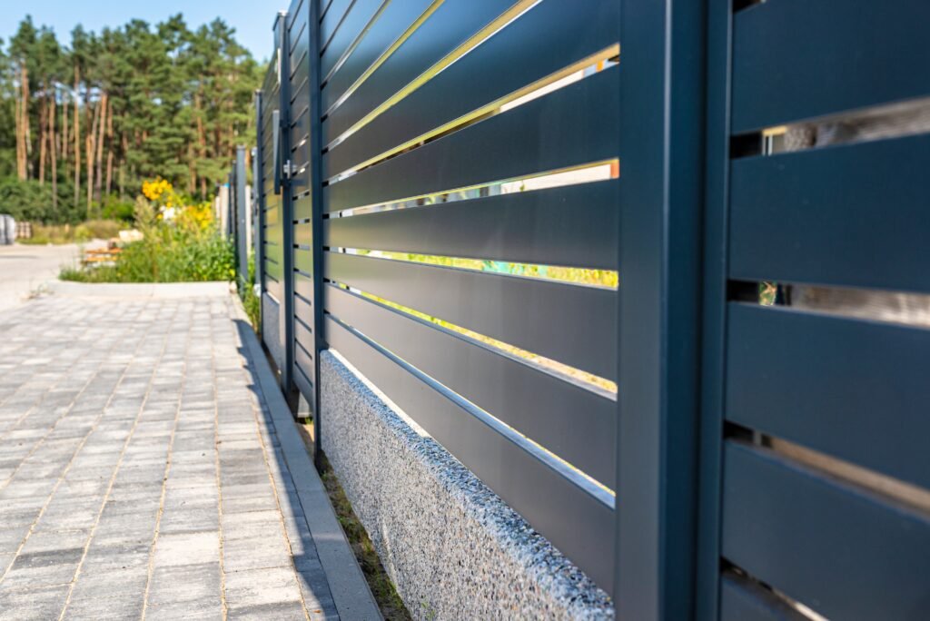 Modern panel fencing in anthracite color, visible spans and a wicket, forest in the background.